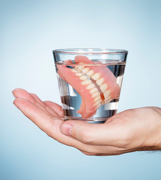 Hand holding glass of water with dentures