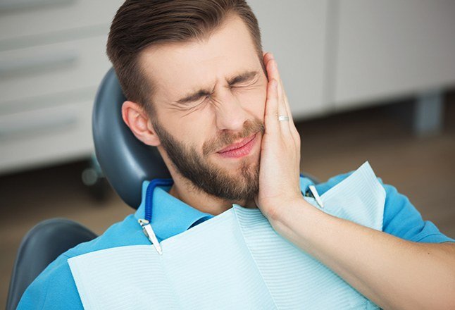 Man who needs to replace missing teeth holding cheek in dental office