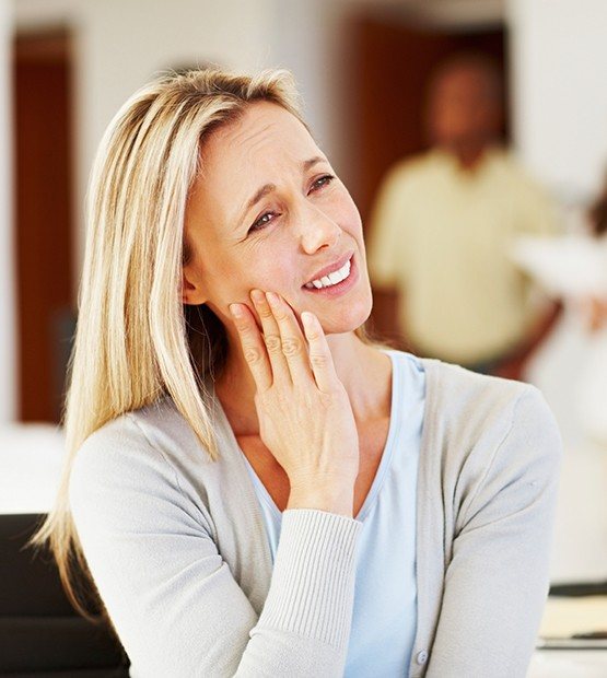 Woman in need of emergency dentistry holding cheek at dental office