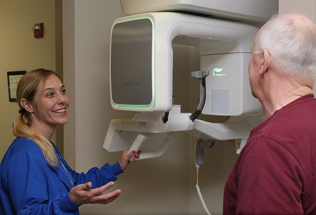 Dental team member showing patient 3 D C T Scanner system
