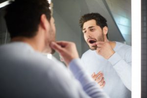 man looking in mirror at his loose dental implant in Flower Mound